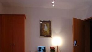 A hotel room with a bed, a desk, a chair, a wardrobe, and a painting on the wall.