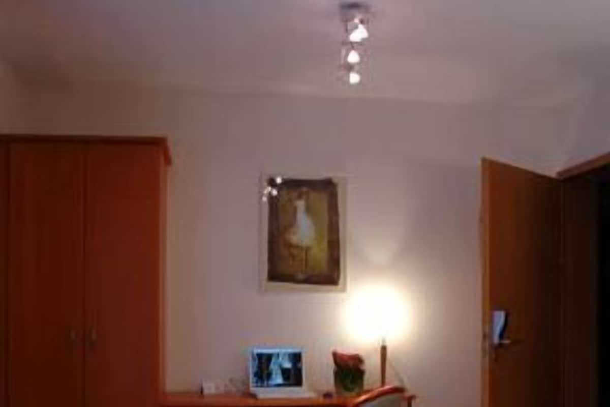 A hotel room with a bed, a desk, a chair, a wardrobe, and a painting on the wall.