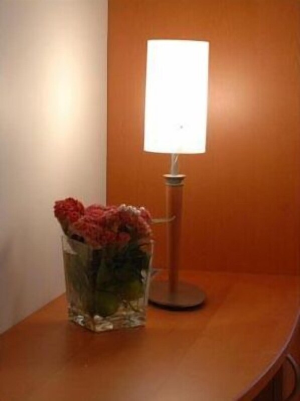 A table with a clear glass vase containing red flowers and a table lamp with a white shade.