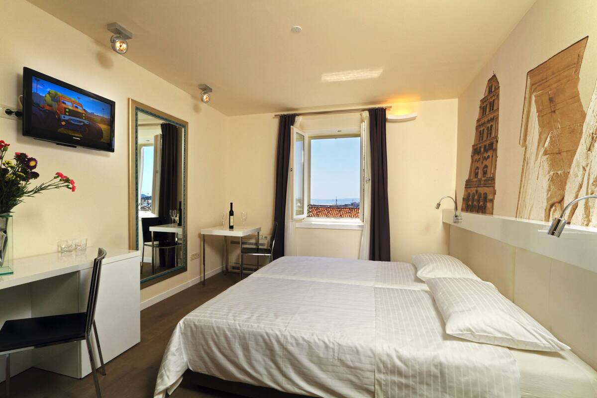 Habitación de hotel con cama, escritorio, televisión, ventana con vistas y un cuadro en la pared.