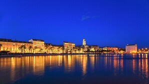 A waterfront cityscape at night with illuminated buildings and a calm river reflecting the lights. - La Porta Luxury Rooms (Split)