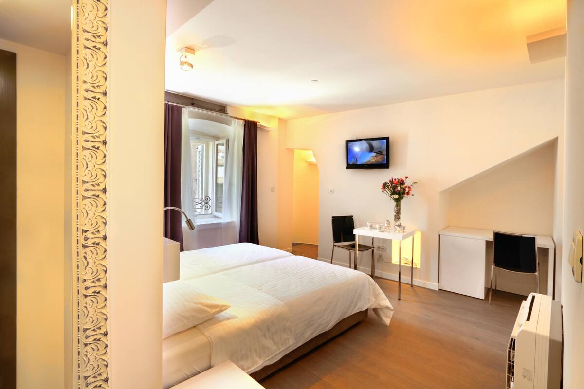 Habitación de hotel con una cama grande, un escritorio con silla, un televisor y una mesita con flores.