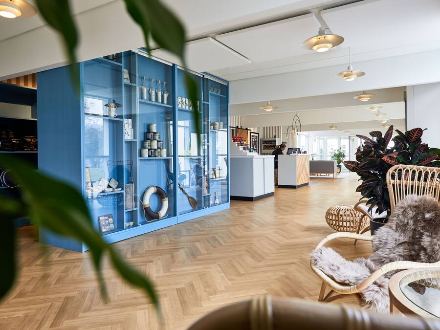 Un hall d’hôtel moderne avec une vitrine bleue, des meubles en osier et un comptoir d’accueil.