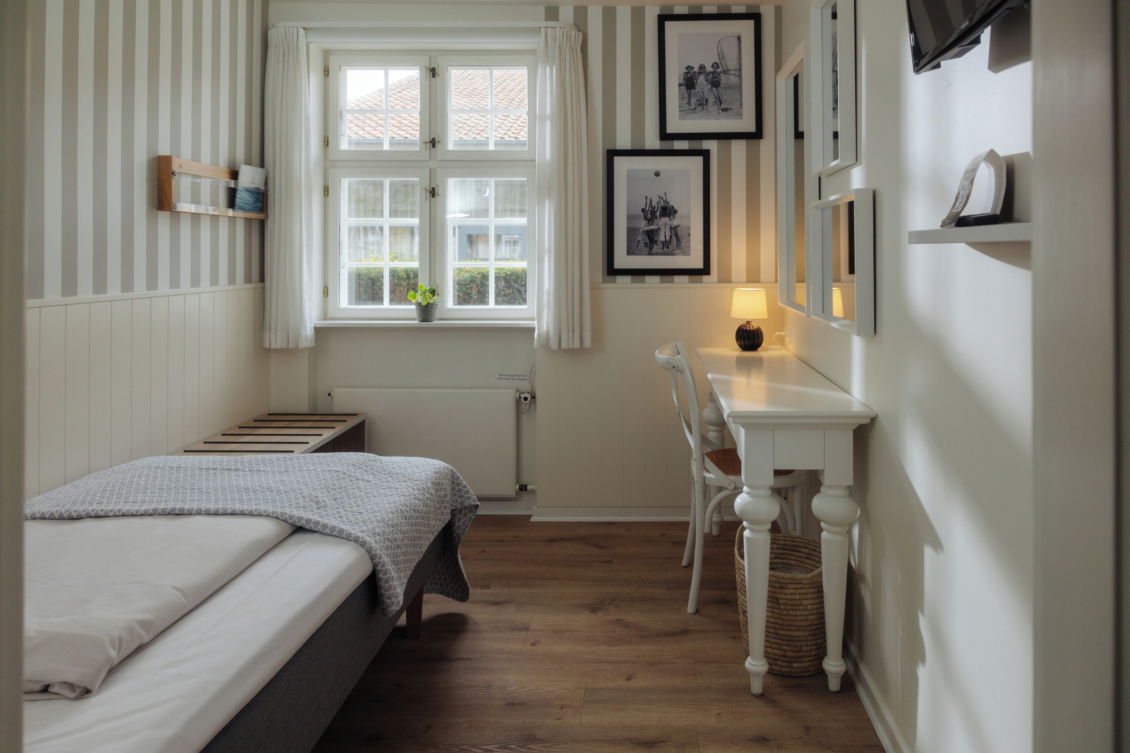 Un dormitorio con cama, escritorio, silla, ventana y radiador.