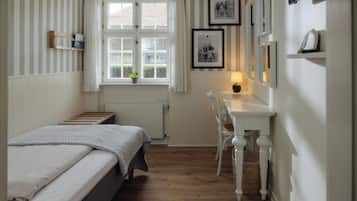 Un dormitorio con cama, escritorio, silla, ventana y radiador.