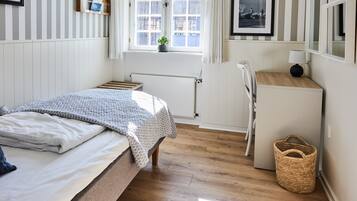 Et pænt opredt soveværelse med seng, skrivebord og et vindue med udsigt til bygninger.