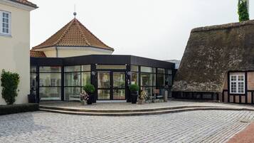 A building with a modern glass entrance, a traditional thatched roof structure, and cobblestone paving.