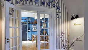 An interior with a wooden herringbone floor, a striped wall, and a door leading to a room with shelves and a table.