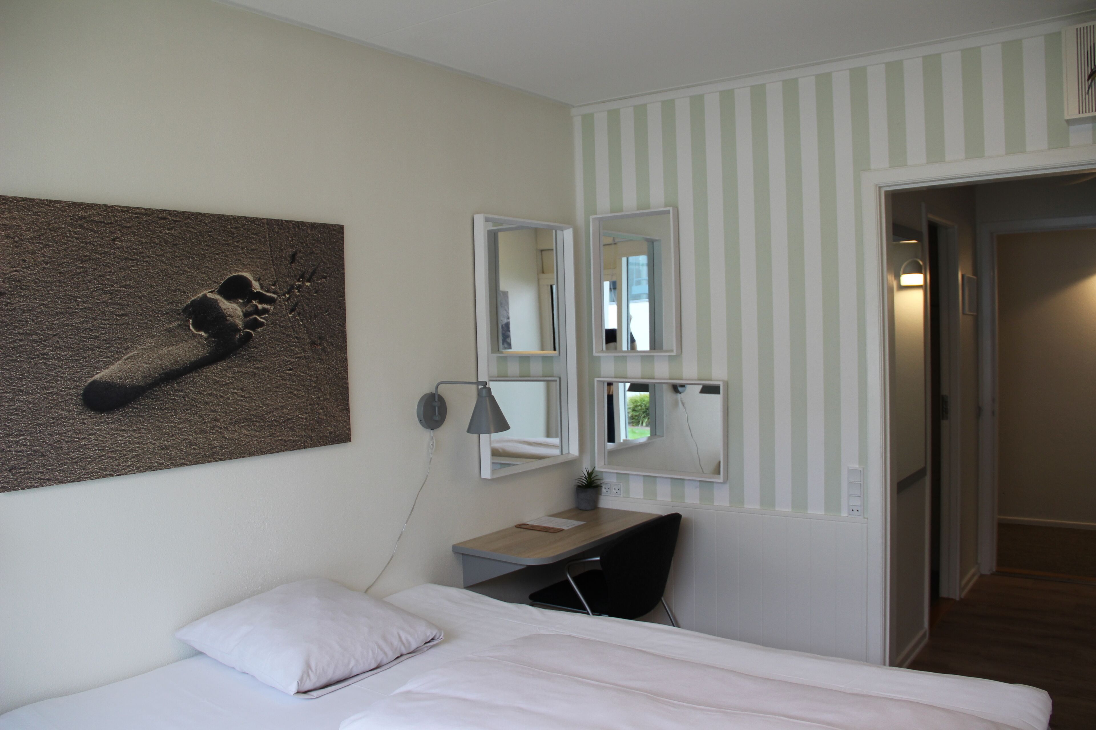 Ein Hotelzimmer mit einem Bett, einem Schreibtisch mit Stuhl, einem Wandspiegel und einem Bild von einem Fußabdruck.