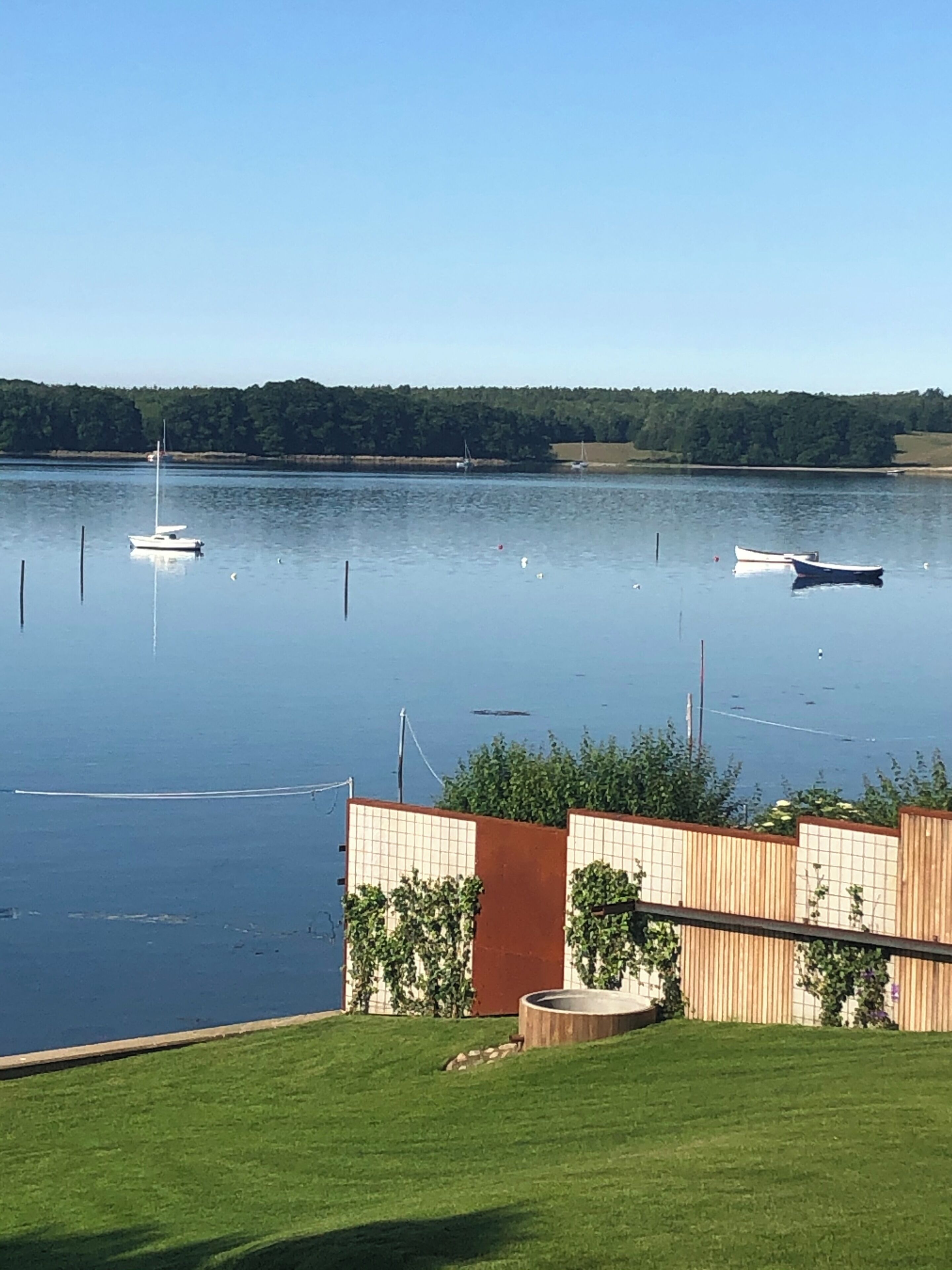 Un lago tranquilo con barcos, una valla de madera y una zona cubierta de césped.