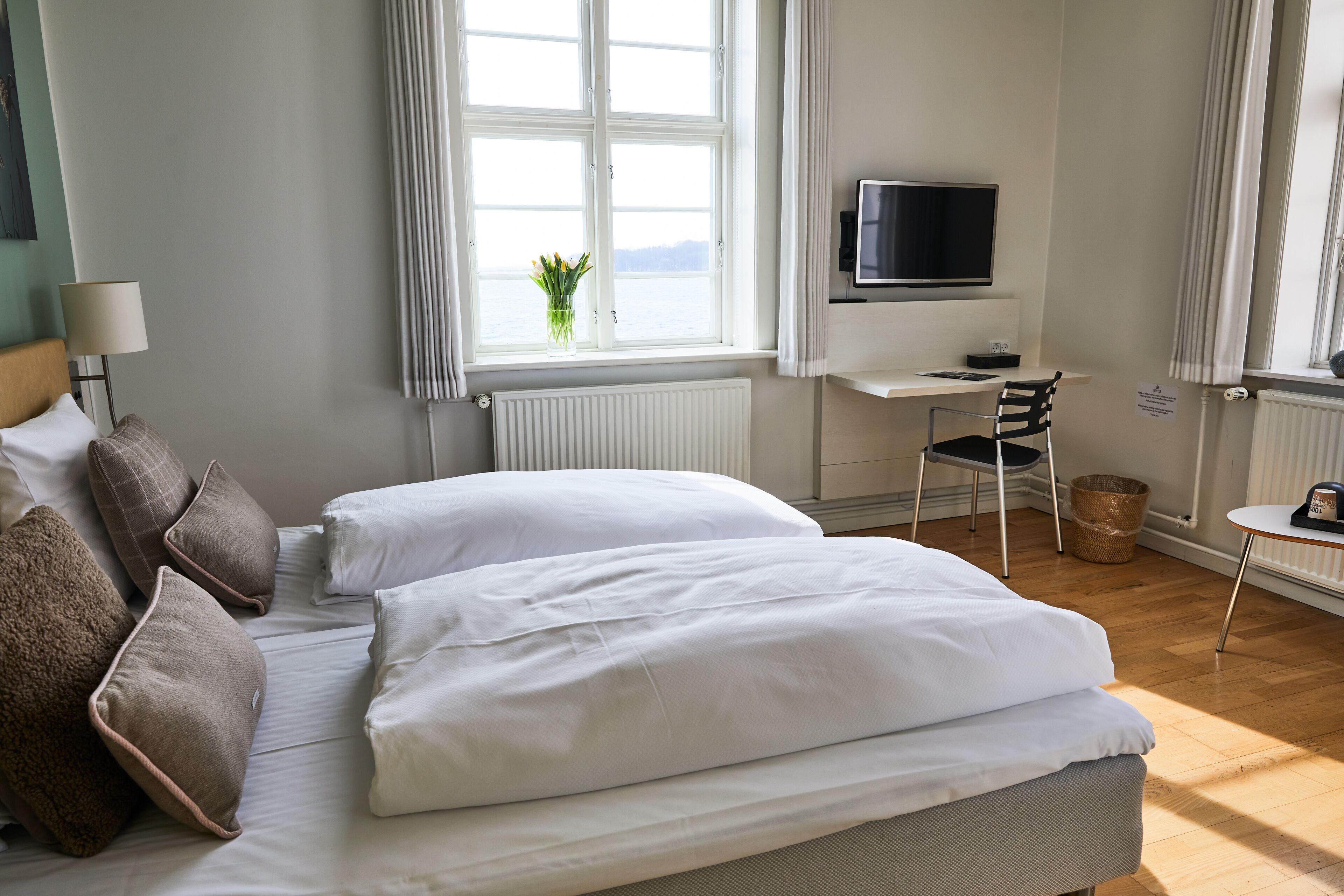 Une chambre d’hôtel bien aménagée, avec un grand lit, un bureau équipé d’un ordinateur, une télévision et une vue sur la mer par la fenêtre.