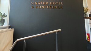 Een zwarte muur met het logo en de naam van Sixtus Sinatur Hotel & Conference.