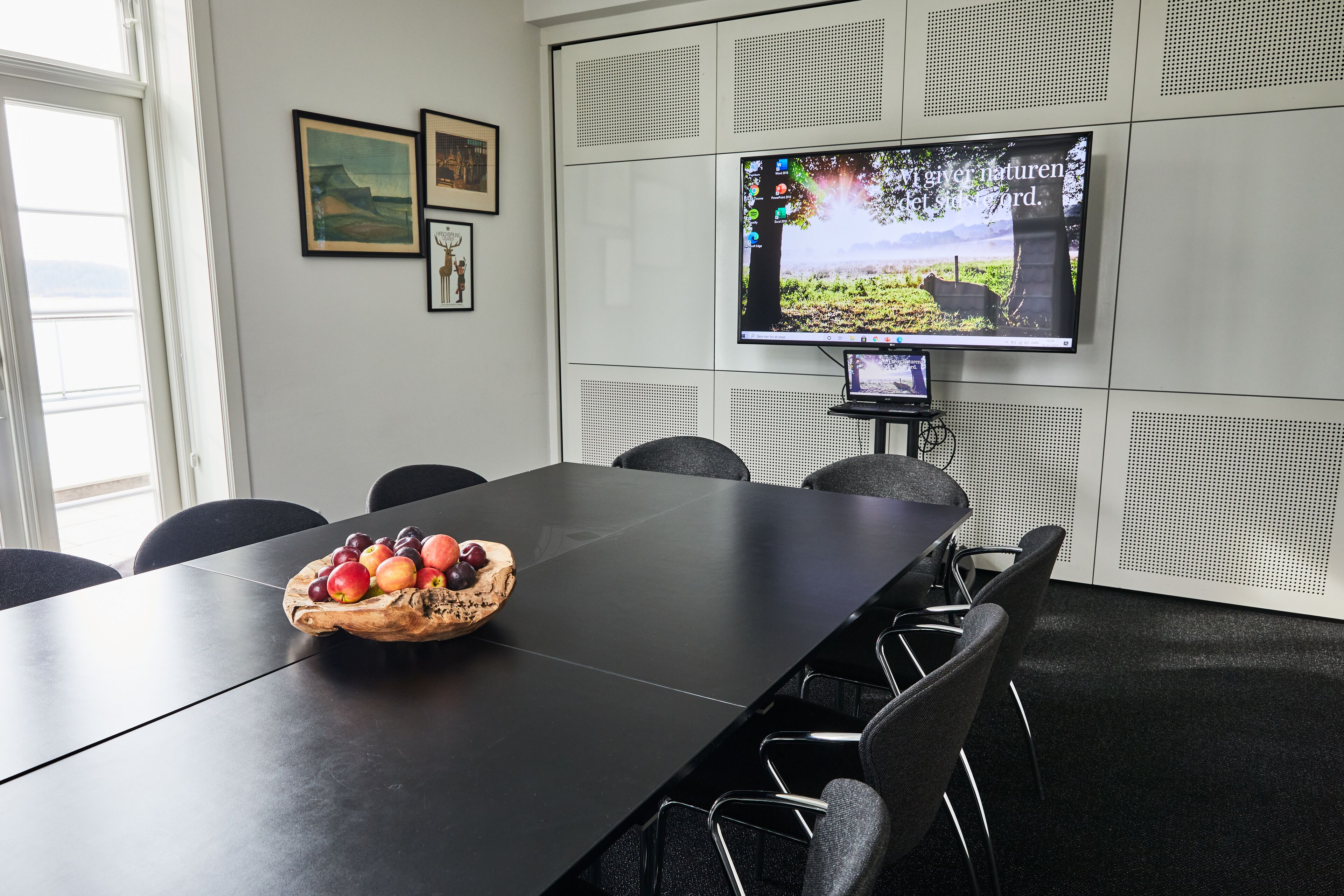 A conference room with a long table, chairs, a fruit bowl, a television on the wall, and soundproofing panels.