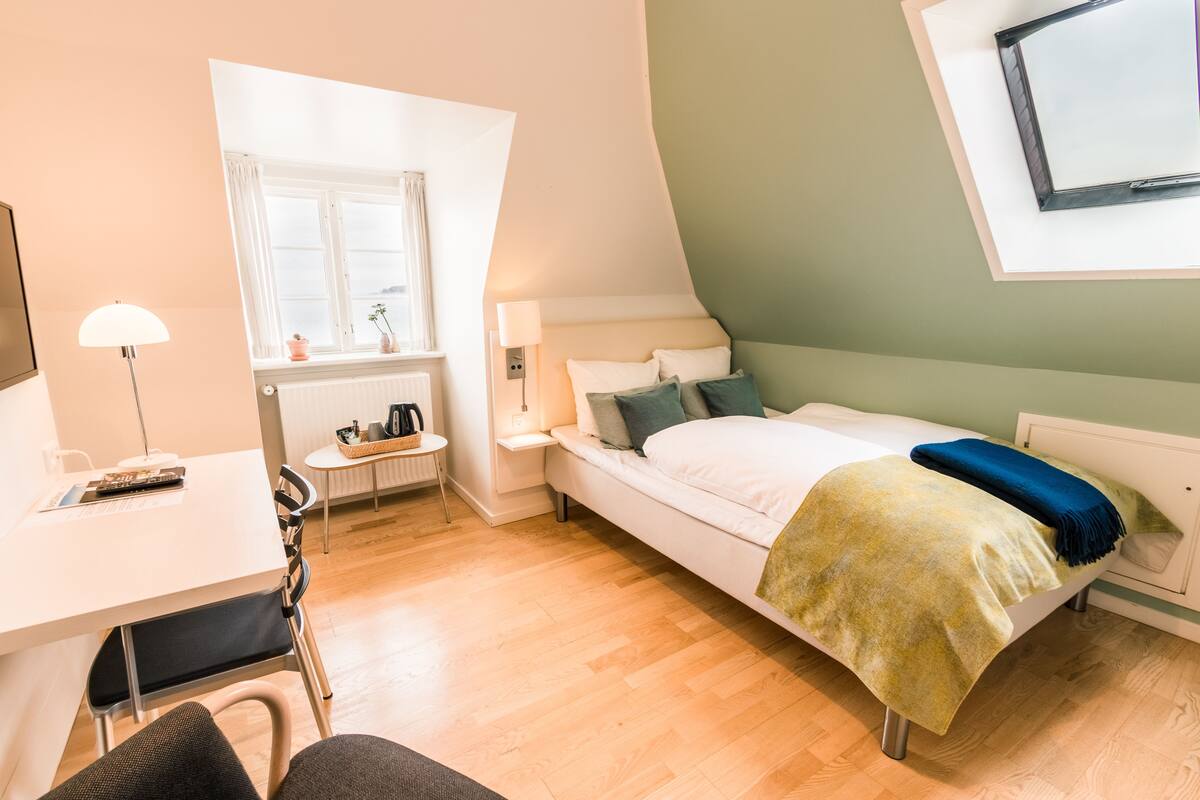 Un dormitorio moderno con cama, mesita de noche, lámpara y ventana con cortinas.