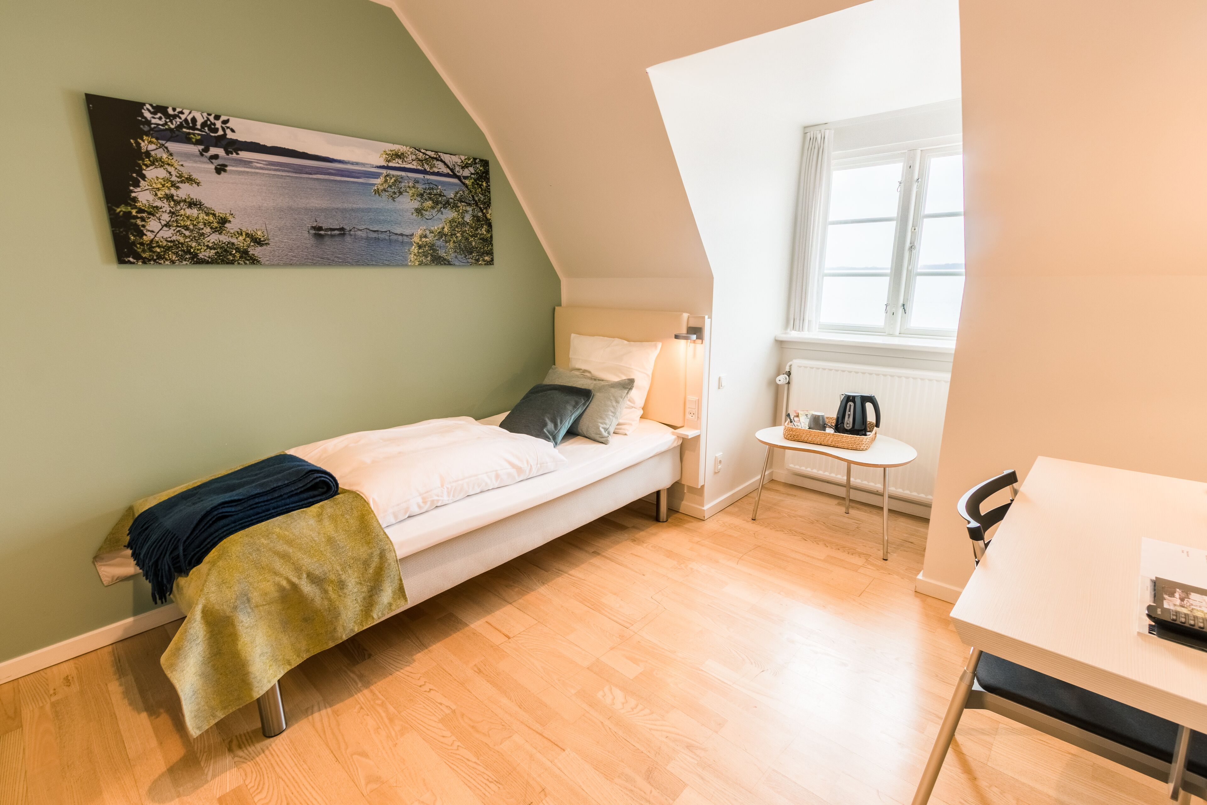 Una habitación pequeña y bien iluminada con una cama, una mesa y un ventanal.