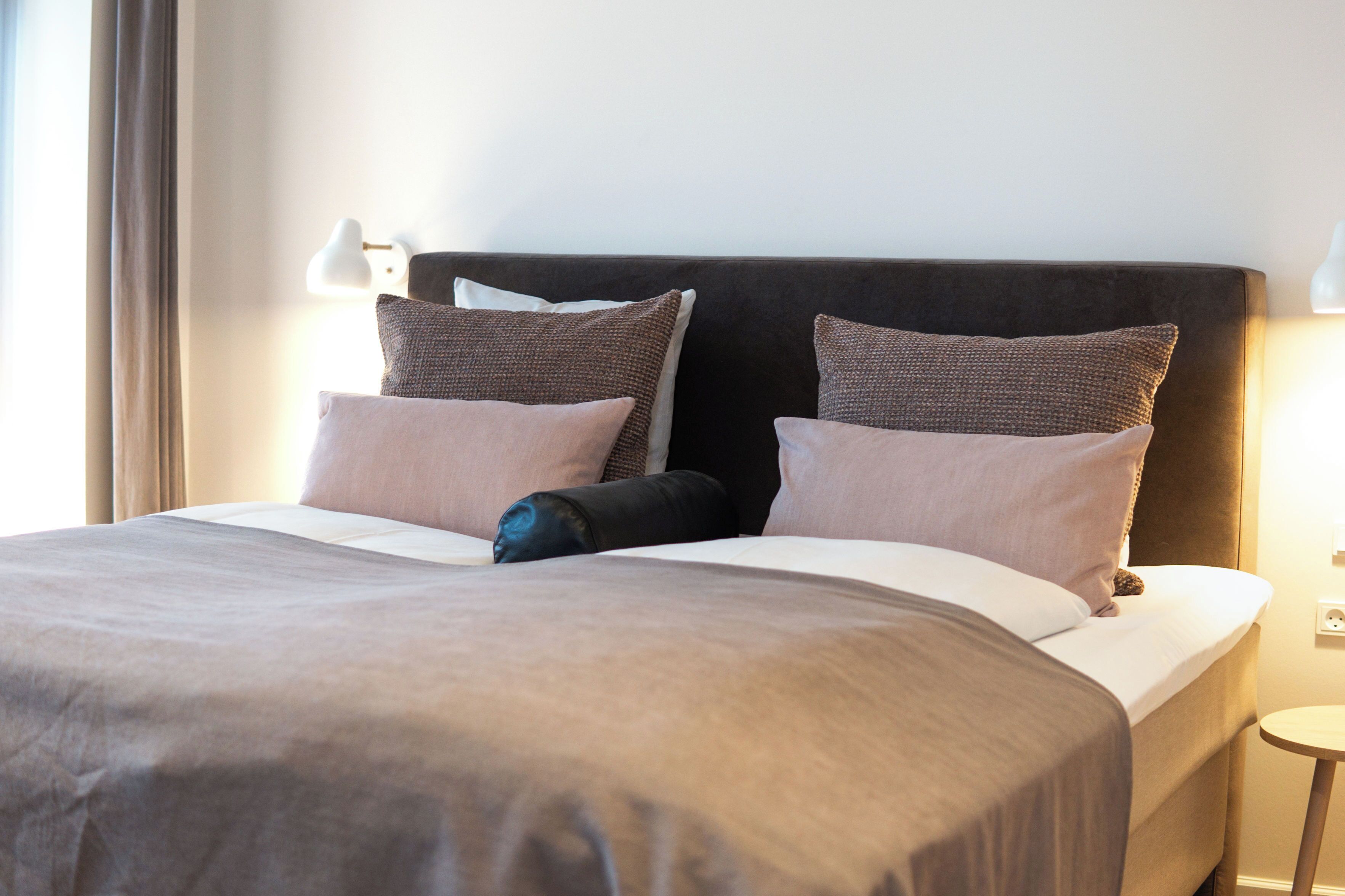 A neatly made bed with a dark headboard, two pillows, and a blanket.