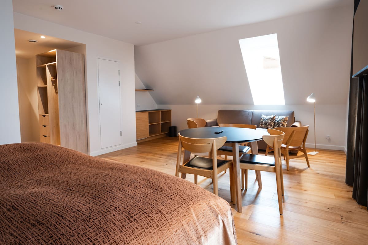 Un dormitorio con una cama grande, una zona de comedor con mesa y sillas, un armario y una ventana que proporciona luz natural.