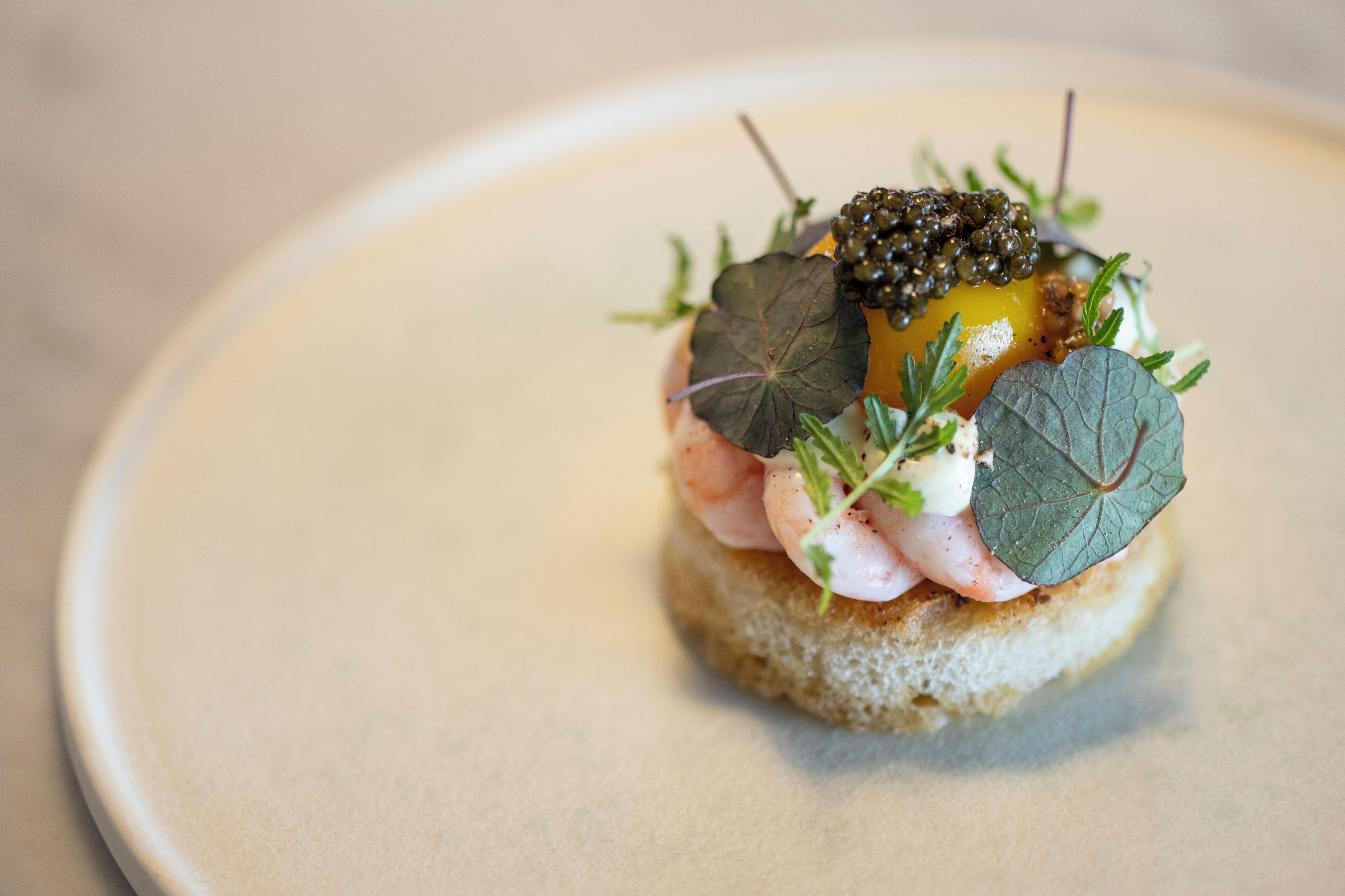 Un plat composé de crevettes, de caviar et de légumes verts, servi sur une tranche de pain.