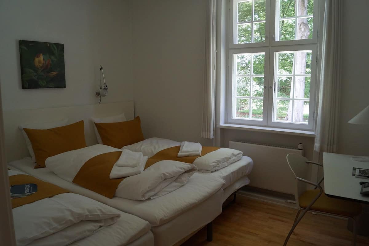 Ein Zimmer mit zwei Betten, einem Schreibtisch und einem Fenster mit Blick auf Bäume.