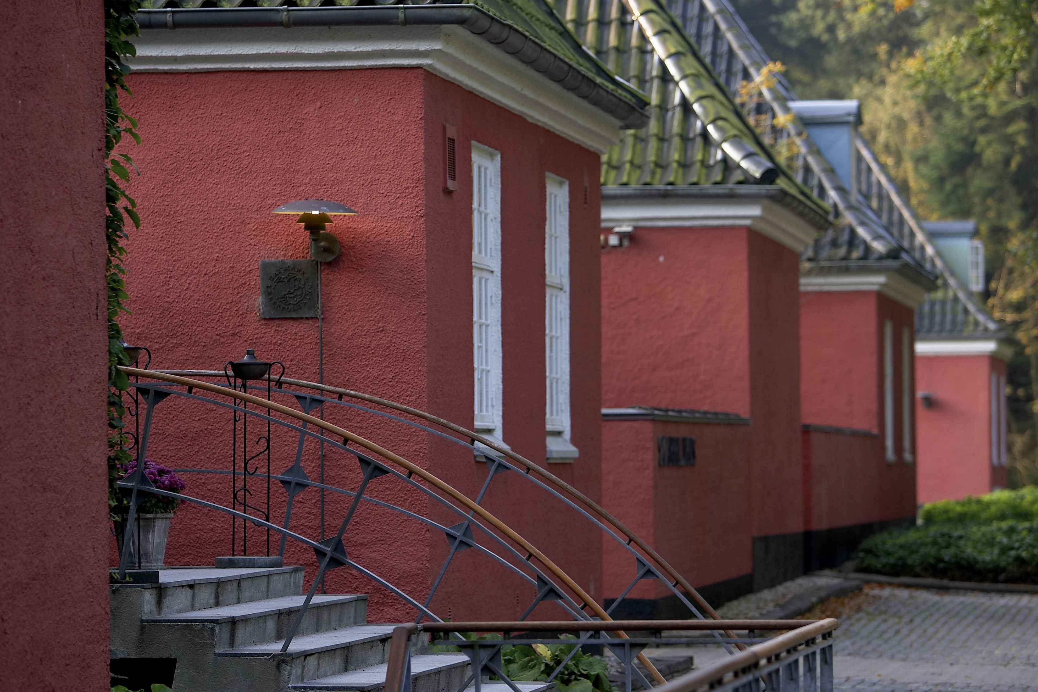 A red building with white window shutters, a metal staircase, and a small garden area.