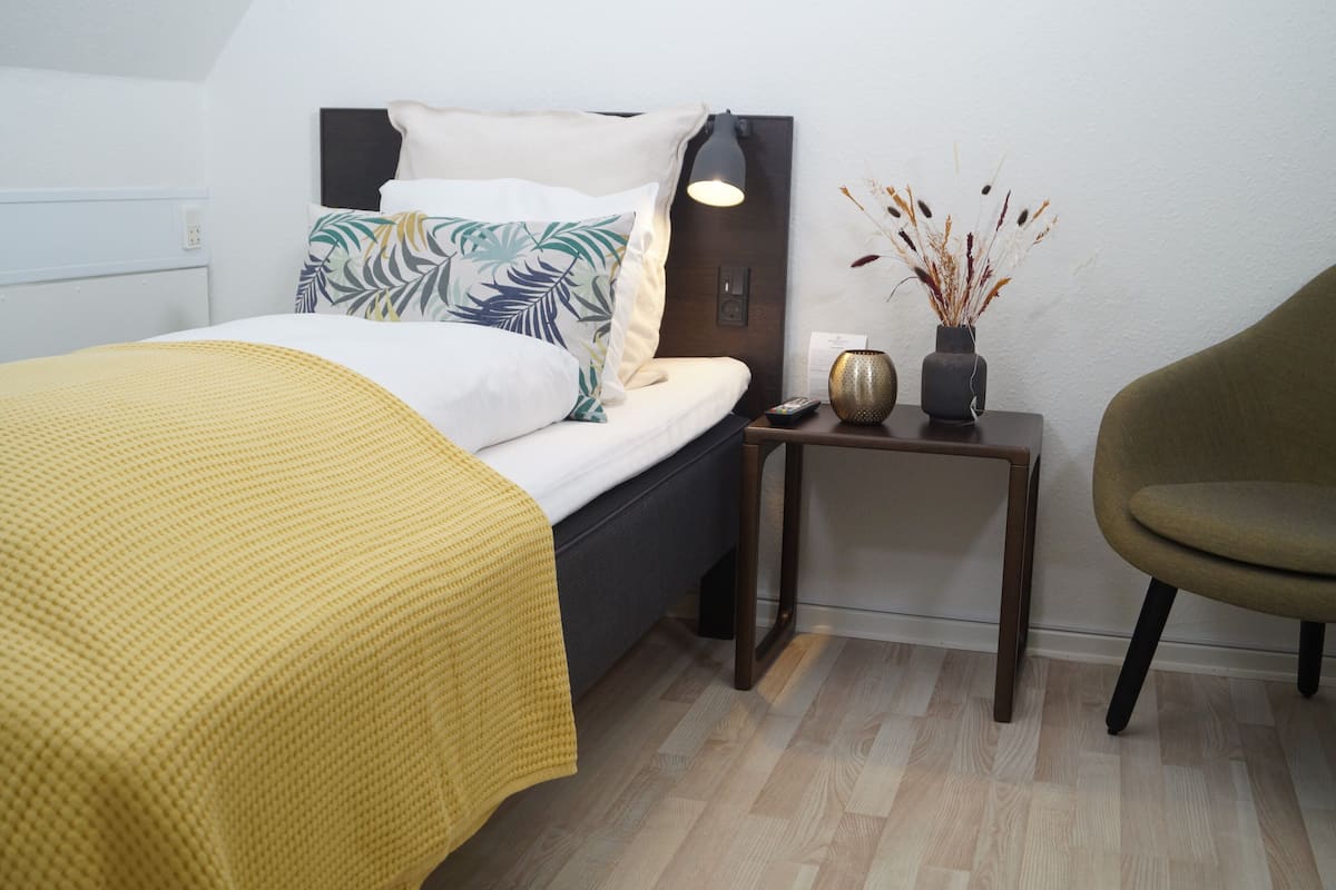 Ein ordentlich eingerichtetes Schlafzimmer mit Bett, Nachttisch, Lampe und Stuhl.