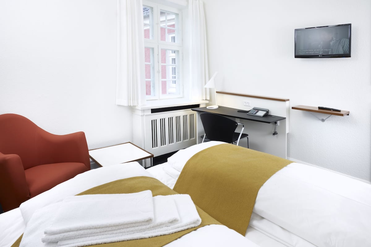 Ein Hotelzimmer mit Bett, Schreibtisch, Stuhl, Fernseher und einem Fenster mit Vorhängen.