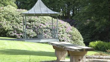 A stone bench in a garden with a gazebo in the background.