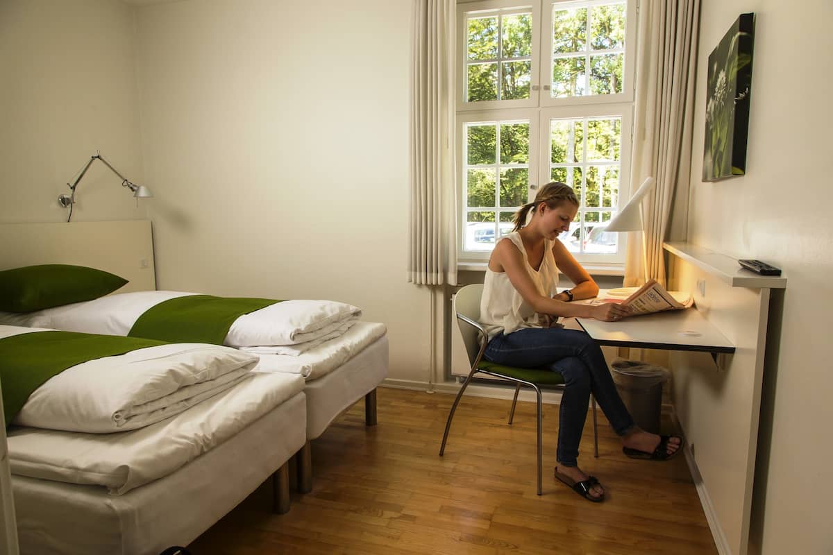 Ein Zimmer mit zwei Einzelbetten, einem Schreibtisch mit Lampe und einem fenster mit Vorhängen.