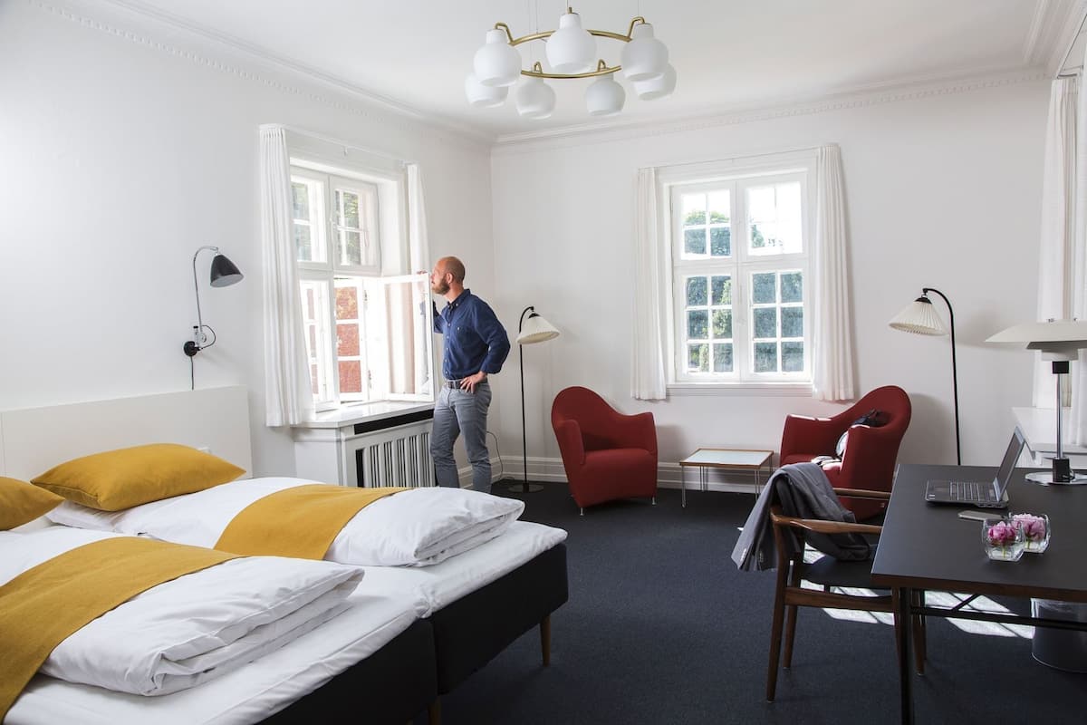 Ein Hotelzimmer mit einem Bett, zwei roten Sessel, einem Tisch und einem Schreibtisch mit einem Laptop.