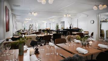 A spacious dining area with multiple tables set for dining, featuring white tablecloths, wine glasses, and cutlery.