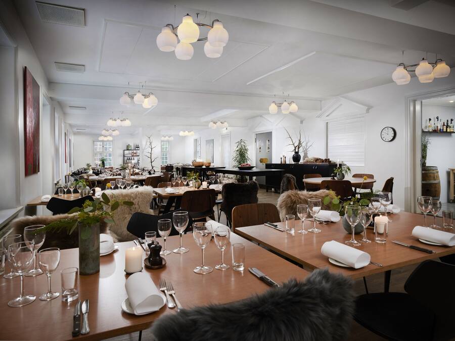 A spacious dining area with multiple tables set for dining, featuring white tablecloths, wine glasses, and cutlery.