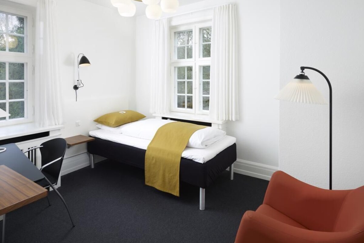 A room with a bed, a desk, a chair, and a lamp.