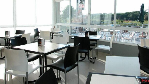 A hotel dining area with tables and chairs, large windows with a view of the outdoors, and a sign indicating the presence of a hotel restaurant. - Hotel Ronsel (Sanxenxo)