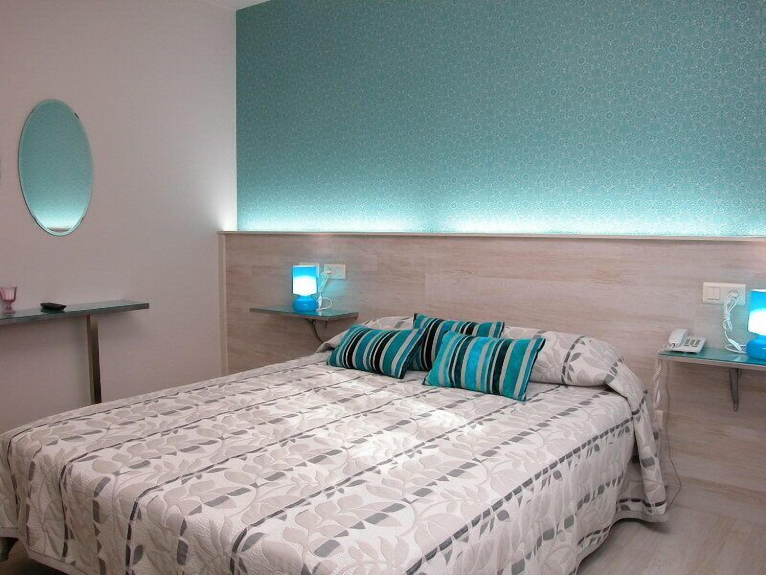 A hotel room with a bed, two bedside tables, a mirror, and a wall with a patterned design.