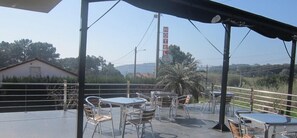 An outdoor patio with metal tables and chairs, a sign for a hotel, and a view of the surrounding landscape. - Hotel Ronsel (Sanxenxo)