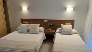 A hotel room with two beds, each with a wooden headboard and white bedding. There are two wall-mounted lights above the beds and a small vase with flowers on the nightstand between the beds. - Hotel Ronsel (Sanxenxo)