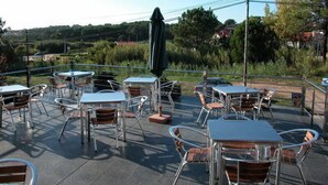 An outdoor patio with tables and chairs, surrounded by greenery and a view of the countryside. - Hotel Ronsel (Sanxenxo)