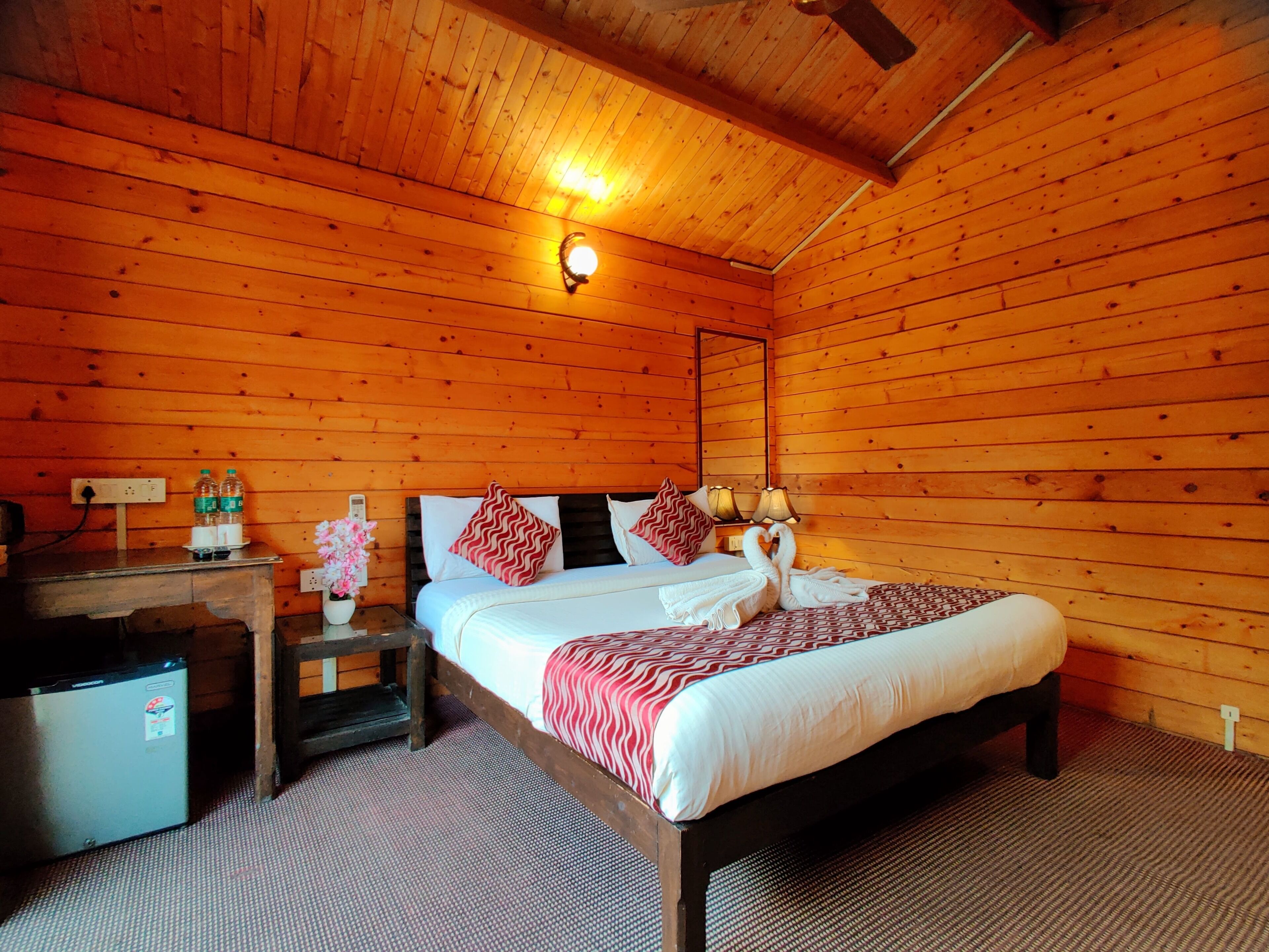 Une chambre dans un chalet en bois, comprenant un lit, des lampes de chevet, une table de chevet, une petite table et un réfrigérateur.
