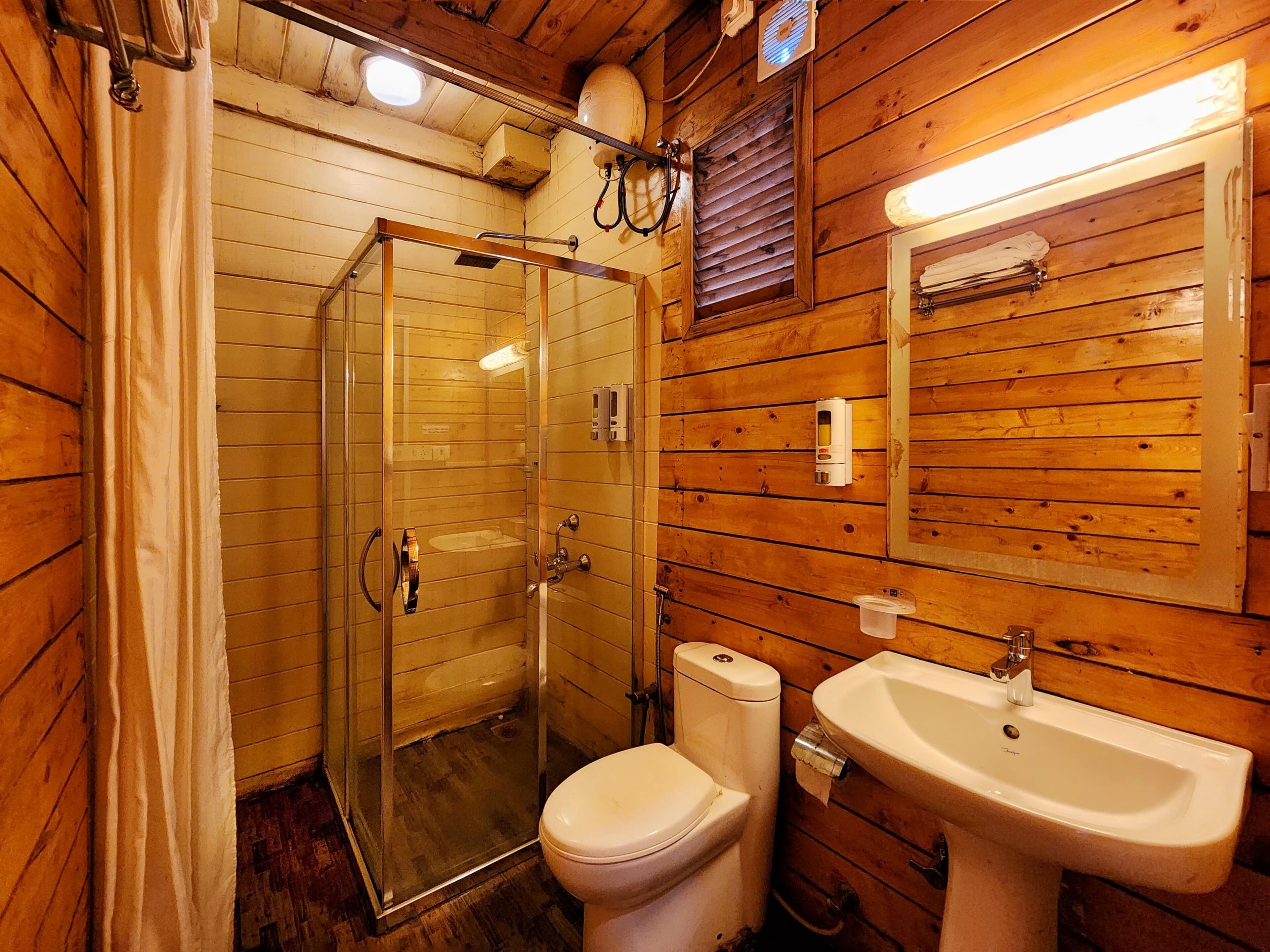 Un baño de cabaña de madera con cabina de ducha de vidrio, un inodoro y un lavamanos.