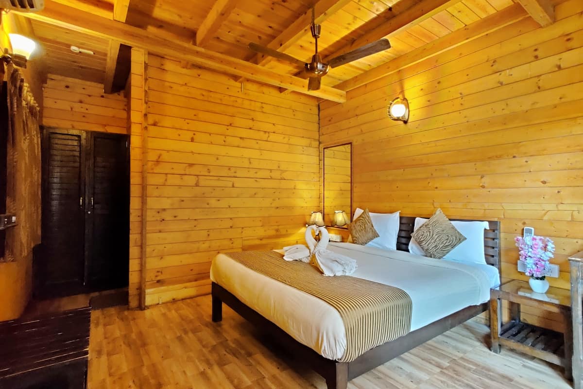 A wooden cabin-style room with a bed, a ceiling fan, and a nightstand with a lamp.