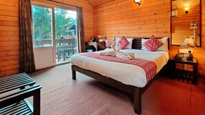 A wooden cabin bedroom with a bed, a nightstand, a mirror, and a view of the outdoors. - La Vie Woods (Calangute)