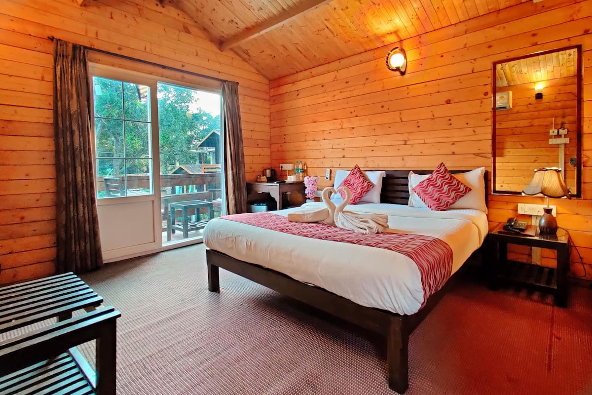 A wooden cabin bedroom with a bed, a nightstand, a mirror, and a view of the outdoors.