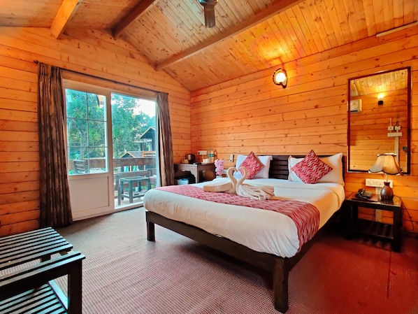 A wooden cabin bedroom with a bed, a nightstand, a mirror, and a view of the outdoors. - La Vie Woods (Calangute)