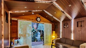 A cozy room with a wooden ceiling, a sofa, a coffee table, and a door leading to a garden. - La Vie Woods (Calangute)