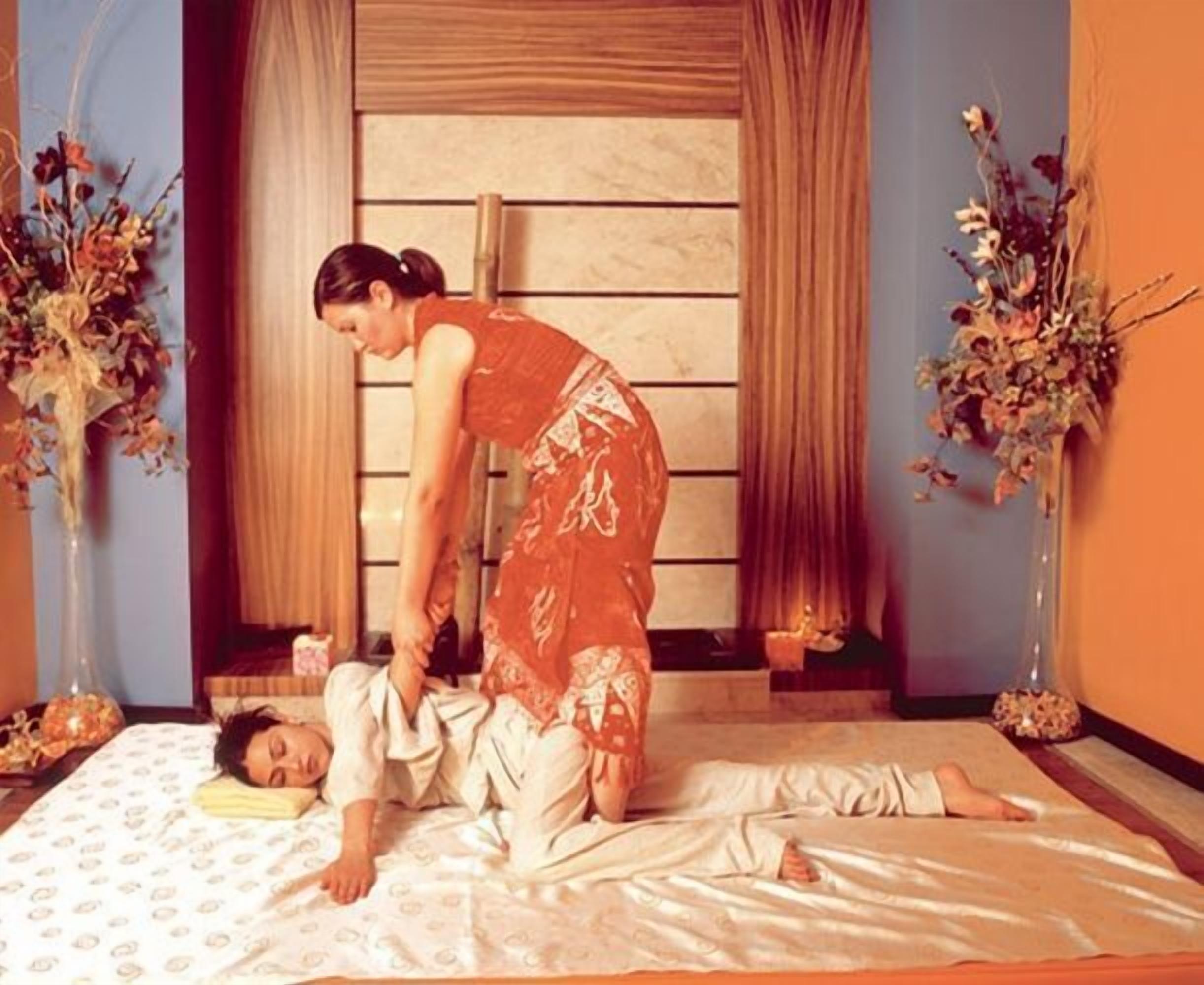 Una habitación con una cama, una persona acostada y otra persona de pie a su lado.
