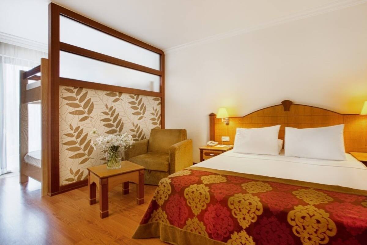 A hotel room with a bed, bedside lamps, a chair, a small table, and a decorative wall panel.