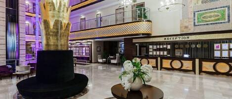 A spacious lobby with a reception desk, a large decorative sculpture, and a chandelier.