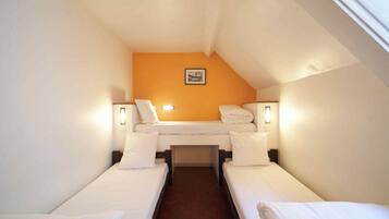 A small, single-room hotel room with two single beds, a small table, and a picture on the wall.