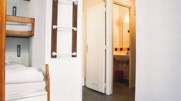 A hotel room with a bed, a wooden shelf, a towel rack, and a bathroom visible through an open door.