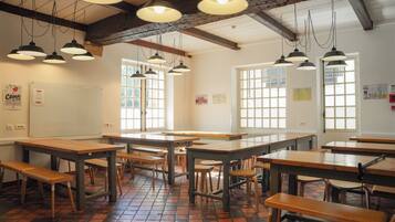 A classroom with wooden tables and benches, large windows, and hanging pendant lights.